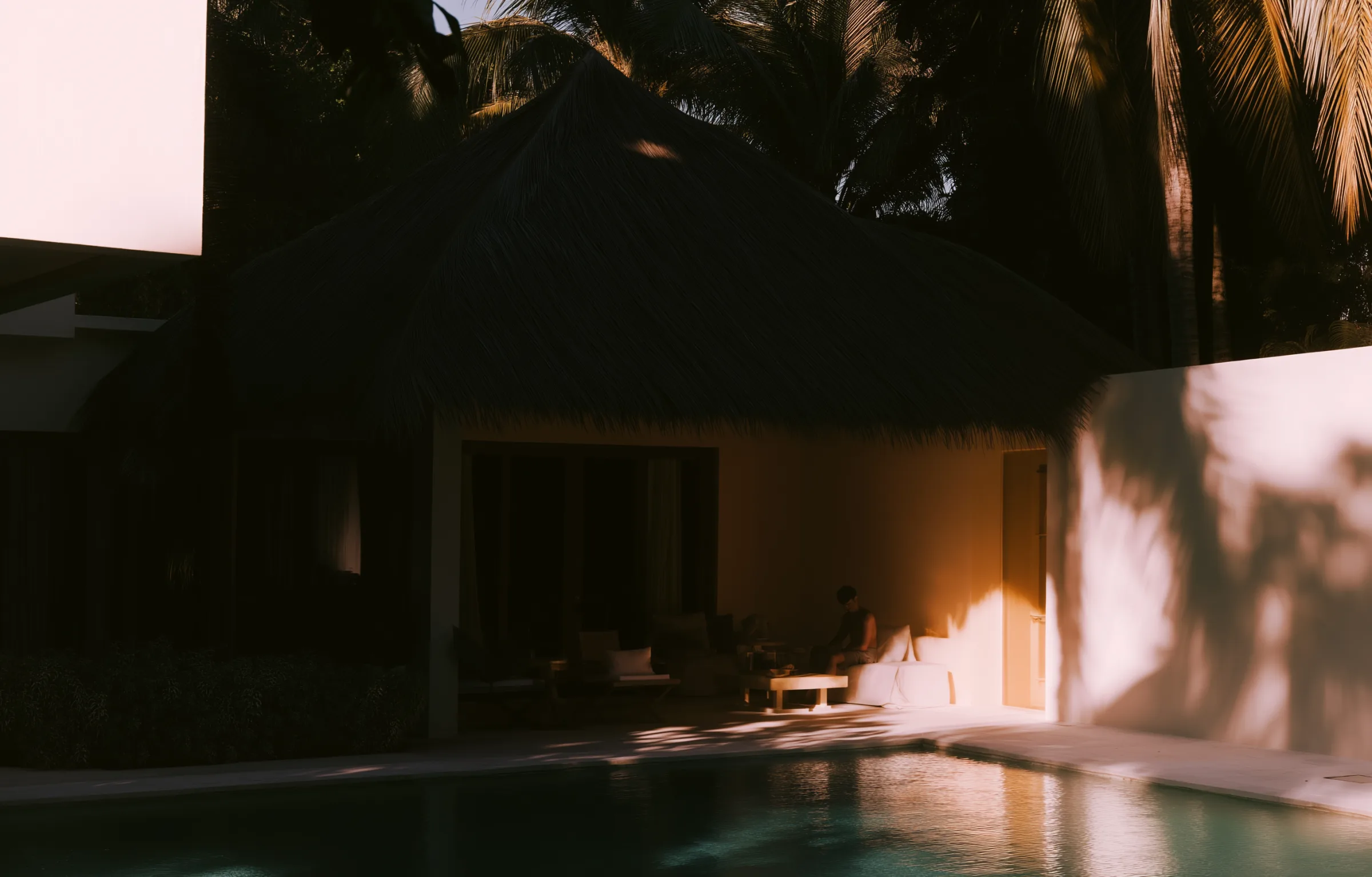 Villa al atardecer con personas trabajando con portátiles junto a la piscina